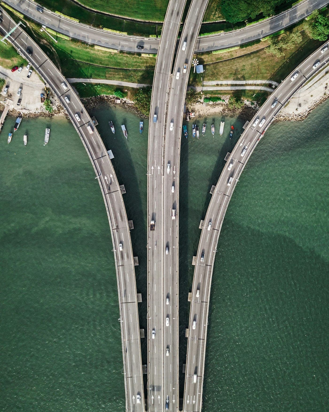 An overhead view of a coastal causeway where a highway divides into three separate carriageways over open water.