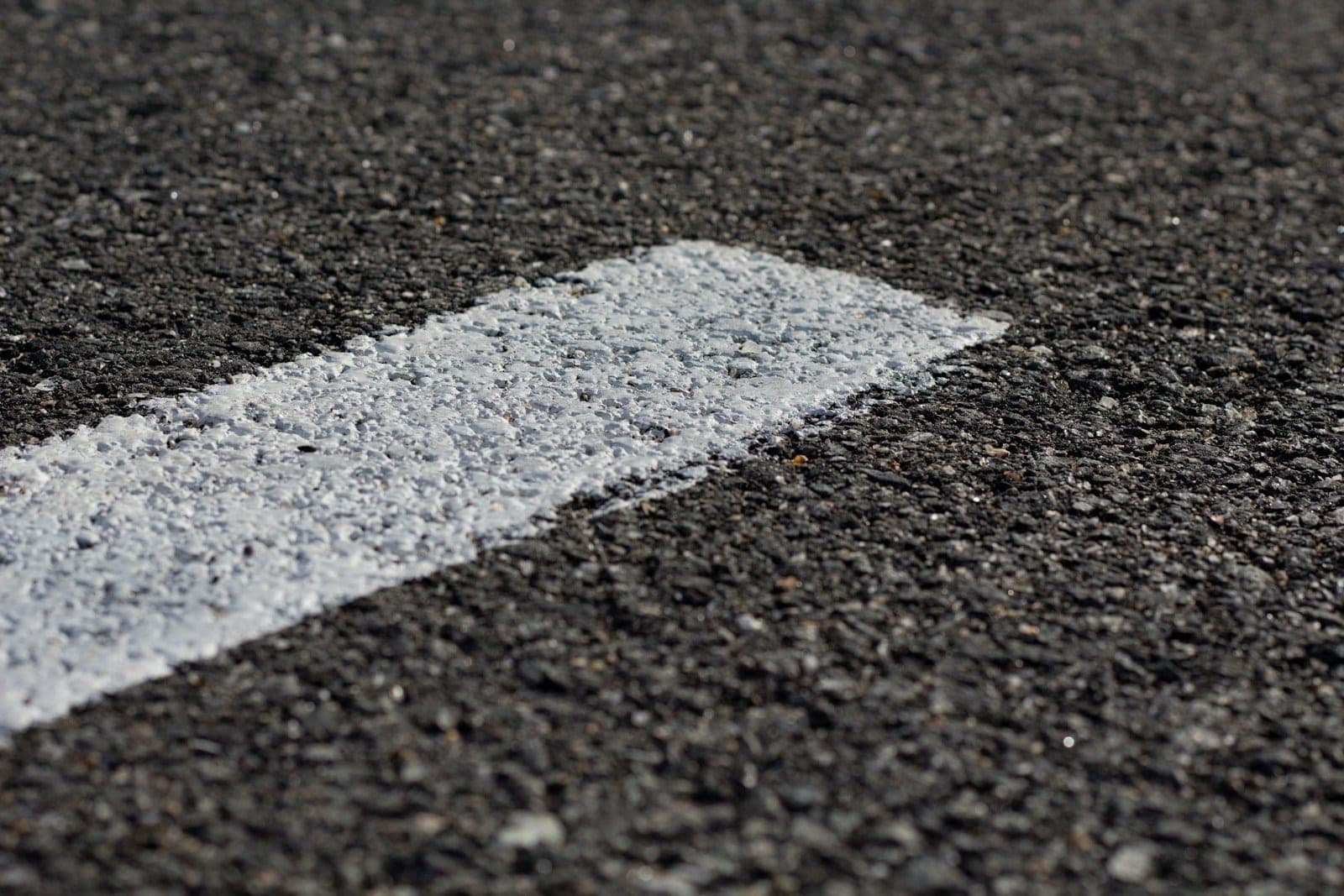 A close view of a painted white lane marking on coarse asphalt.